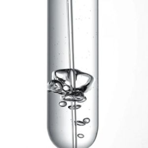 Close-up of a transparent skincare serum inside a glass laboratory-style tube, featuring suspended bubbles and a smooth liquid texture against a light background.